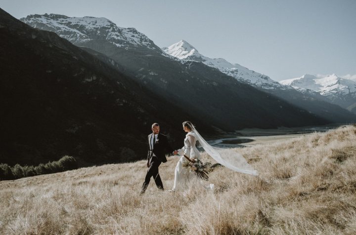 Midge Edine Photography Wild Hearts Wedding Vendor Directory -  whose craft is capturing those special in between moments, and making memories out of feelings - bride and groom walking in field with mountains in background