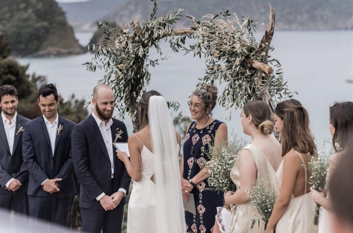 Married by Sian Wild Hearts Wedding Vendor Directory -  an Independent Marriage Celebrant based in Nelson offering couples a fresh and flexible approach to planning their ceremony - Sian in front of bride and groom and bridal party under floral archway